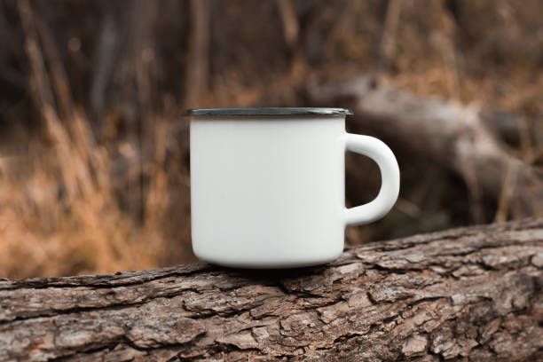 istock White blank metal mug mock up standing on tree outdoors, autumn forest behind. Enamelled travel cup with empty space for logo or branding 1348836703