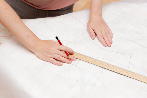 Female hands do the layout of the sewing pattern on paper Female hands do the layout of the sewing pattern on paper. Close Up clothing pattern stock pictures, royalty-free photos & images