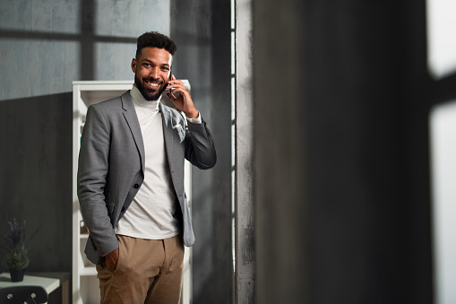 A happy young african american businessman with martphone indoors in office, looking at camera.