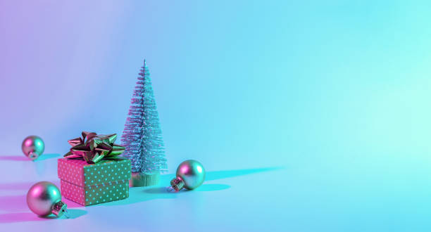 istock Neon Christmas winter background. Minimal abstract tree, xmas gift box. Holiday decoration bauble ball on neon gradient backdrop. Happy new year copy space. 1348845129