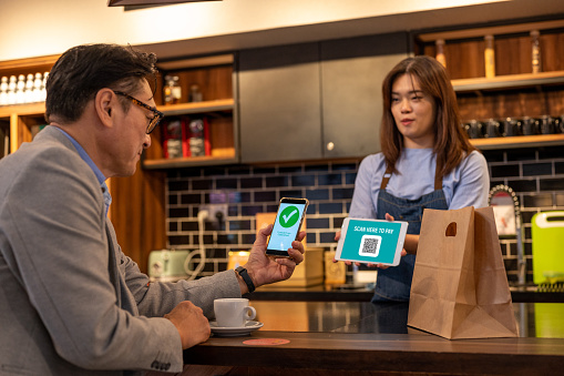 An Asian businessman using smart phone for paying contactless at coffee shop.
Waiter Showing Contactless Menu To Customer.