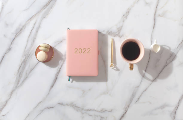 istock Pink coral colored diary for the year 2022, pen, coffee, macaron cookie. Marble background 1348845317