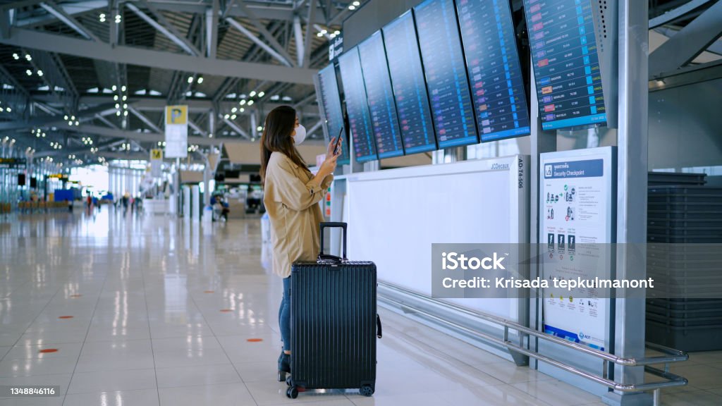 Business woman wear surgical mask checking boarding time at digital timetable. Asian business woman wear surgical mask checking boarding time at digital timetable at the airport terminal. Airport Stock Photo