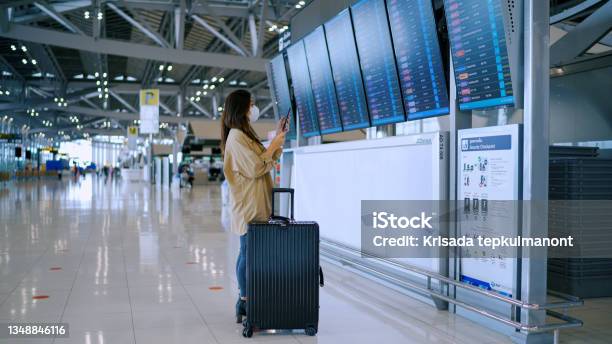 Business Woman Wear Surgical Mask Checking Boarding Time At Digital Timetable Stock Photo - Download Image Now