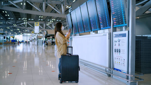 kobieta biznesu nosi maskę chirurgiczną sprawdzając czas wejścia na pokład w cyfrowym rozkładzie jazdy. - commercial airplane airport arrival departure board business travel zdjęcia i obrazy z banku zdjęć