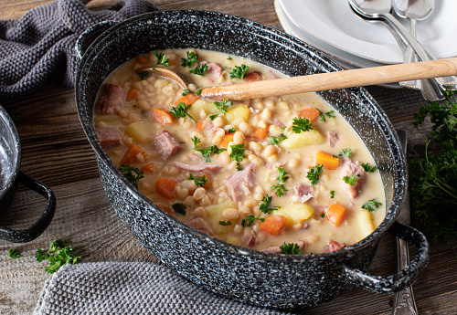 Delicious homemade cooked pot with stew. Made with cured pork, white beans, potatoes and root vegetables. Served on rustic and wooden table from above.