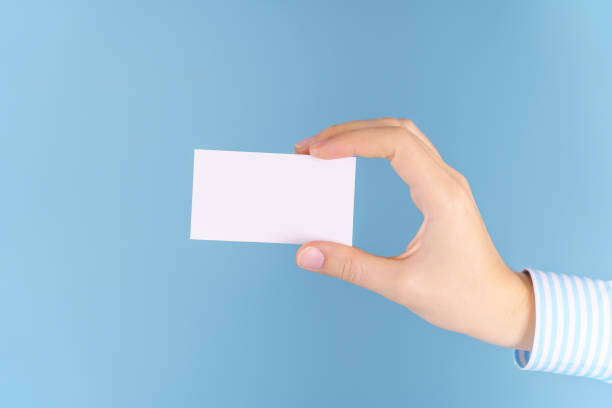 istock A woman's hand holds a white empty business card on a blue background, a mockup 1348853475