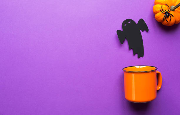 istock Orange mug on a purple background with terrible Halloween decorations. The concept of the Halloween holiday. Drink, fun, party. Copy space, mock up, flatly 1348856472