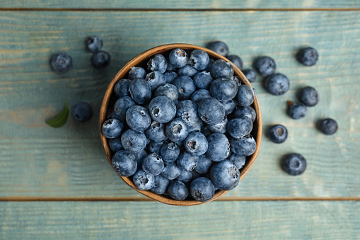 Fresh ripe blueberries in bowl on wooden table, flat lay