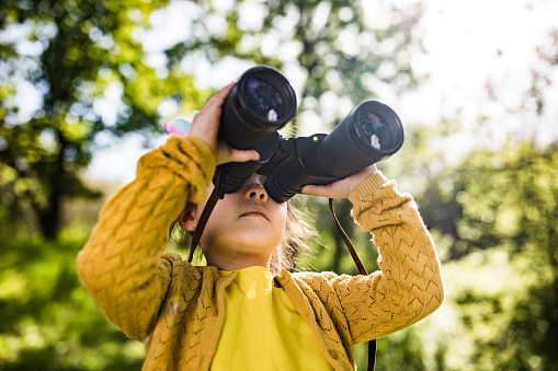 Small girl enjoying while looking through binoculars at the park.