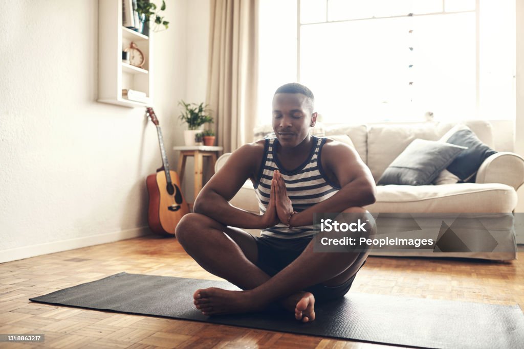 Shot of a sporty young man meditating at home Your thoughts control your life Meditating Stock Photo