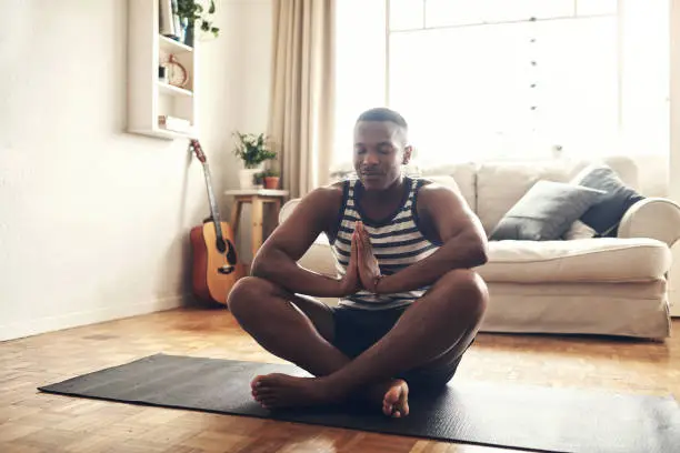 Photo of Shot of a sporty young man meditating at home