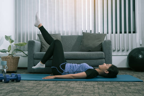 istock Asian woman practicing yoga at home while lying on a mat and stretching her legs. 1348863408
