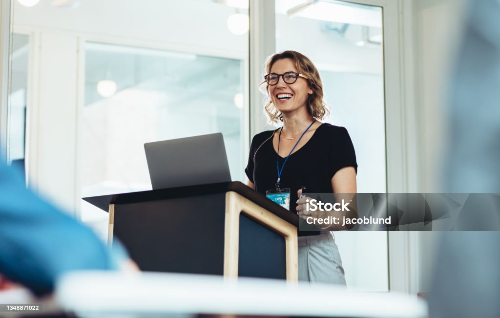 Female business professional addressing a seminar Businesswoman standing at podium with laptop giving a speech. Successful female business professional addressing a seminar. Public Speaker Stock Photo