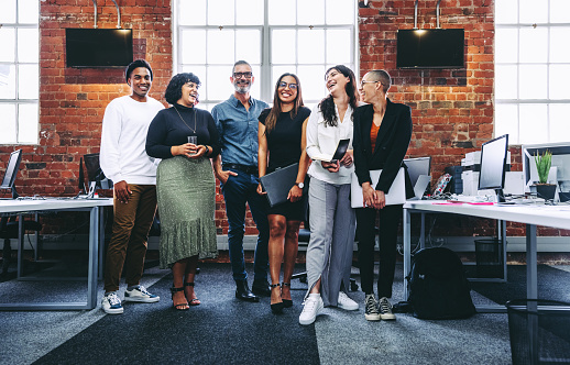 Happy group of businesspeople laughing cheerfully in a modern workplace. Diverse group of colleagues enjoying working together in an office. Successful businesspeople standing together.