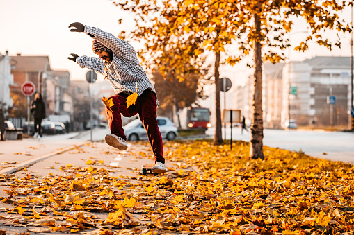 Young Caucasian skateboarder falling from his skateboard on sidewalk. Autumn time.