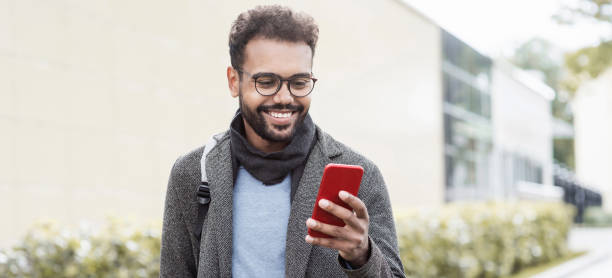 istock Handsome young man wearing warm clothing using smart phone in a city, panoramic banner 1348876067
