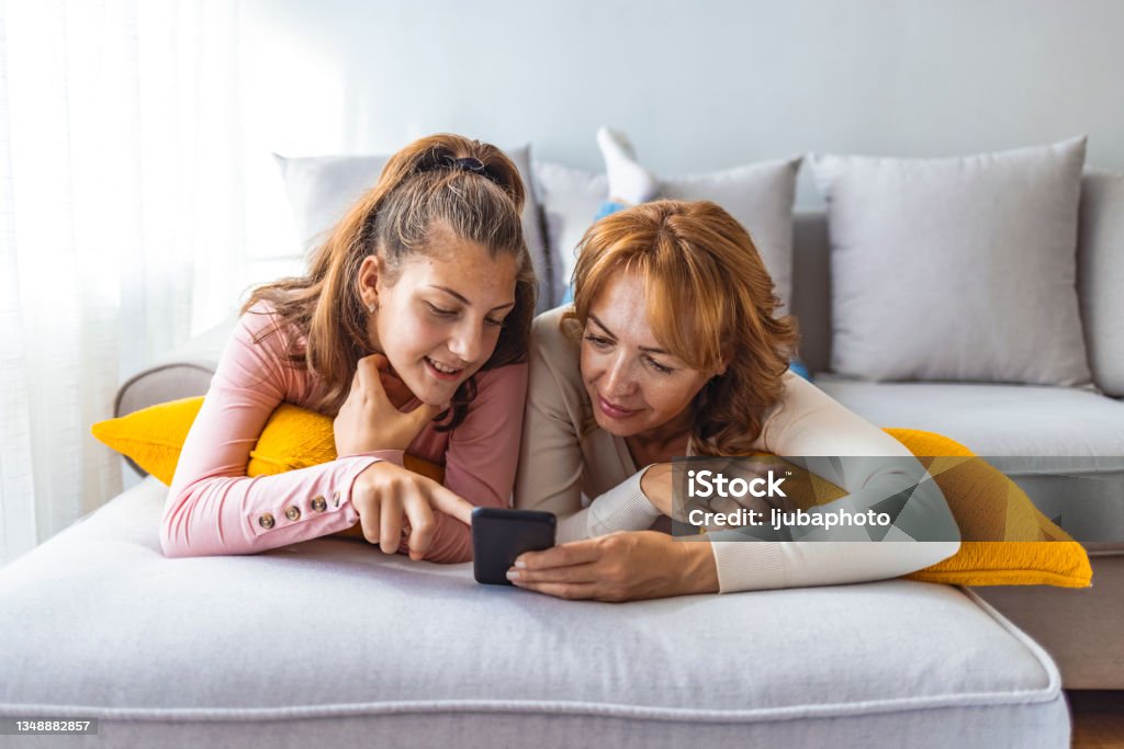 Mother and daughter using a smartphone Mother and daughter laying on a couch at home using a smartphone Teenager Stock Photo