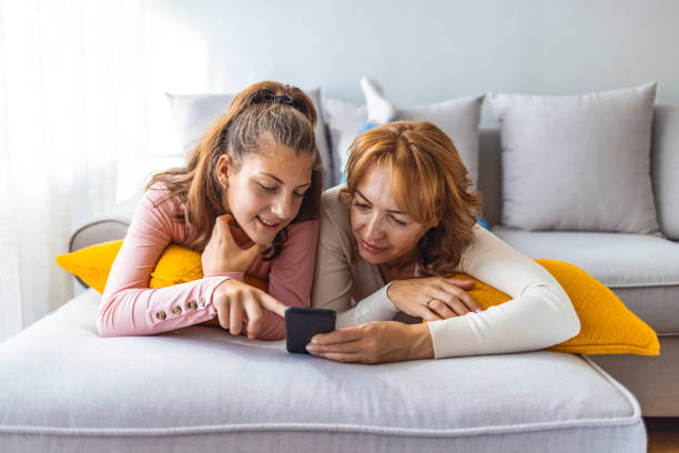 mother and daughter using a smartphone - education relaxation women home interior imagens e fotografias de stock