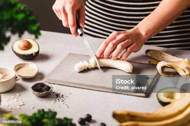 Woman Chopping Banana For Making Smoothie Bowl In Kitchen Stock Photo - Download Image Now