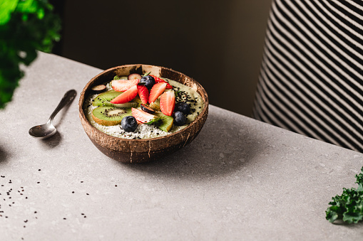 Banana smoothie bowl with chopped kiwi and strawberries, blueberries, and black sesame seeds over kitchen counter.