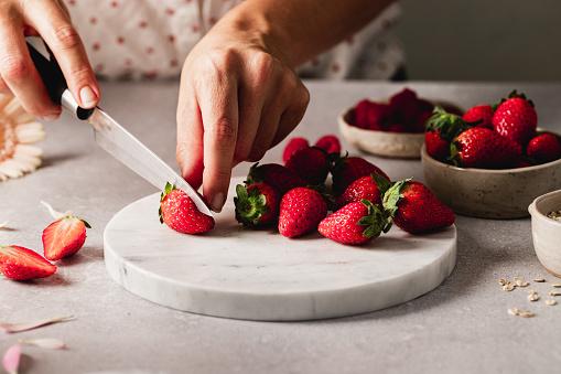 Female hands cutting strawberry on chopping board in the kitchen. Woman cutting fresh strawberries.