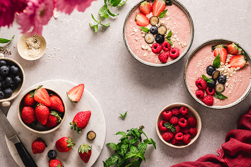 Top view of a strawberry smoothie bowls on the kitchen counter. Strawberries, mint leaves, raspberry, roasted oats, with two bowls of smoothie.