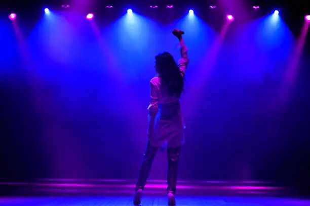 Photo of Cool singer with microphone on bright backlit stage in bright blue lights