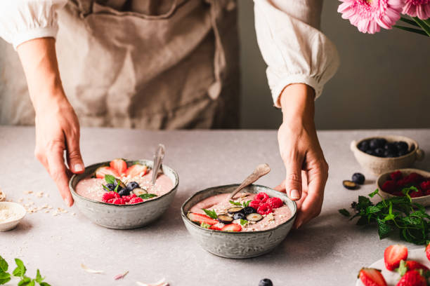 Woman preparing strawberry smoothie bowl in kitchen Woman preparing strawberry smoothie bowl in kitchen.  Close-up of a female hands making smoothie bowls with ingredients on table. blended drink photos stock pictures, royalty-free photos & images