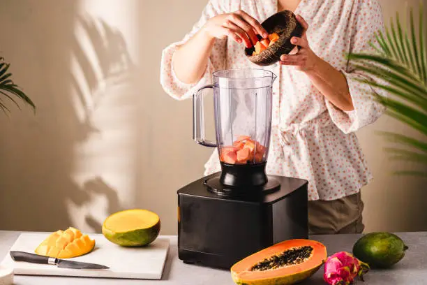 Woman preparing smoothie in the kitchen. Female adding fruits in a blender for making a smoothie at home.