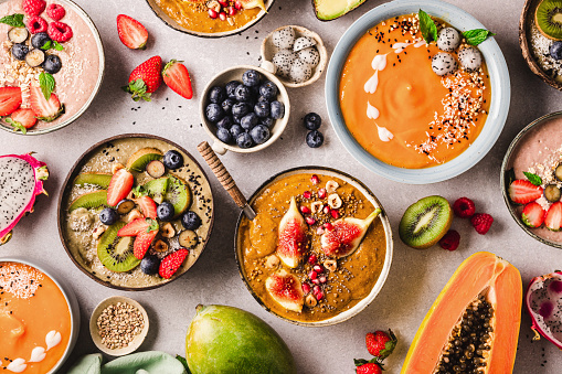Variety of healthy smoothie bowls with ingredients on the kitchen counter. Top view of different types of fruit smoothie bowls served on table.