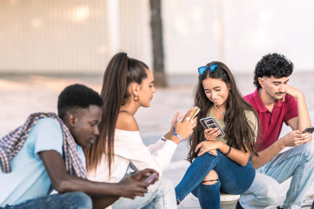 istock Young people of different ethnicities sitting outdoors looking at their mobiles 1348888803