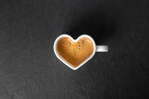 tasse blanche en forme de cœur avec du café et une belle mousse sur un fond de pierre noire. vue d’en haut. espace de copie - black coffee coffee macro cafe photos et images de collection