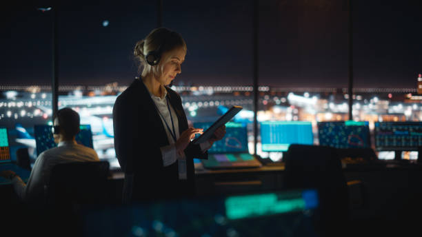 caucasian female air traffic controller working on tablet in airport tower. office room is full of desktop computer displays with navigation screens, airplane flight radar data for the team. - air vehicle audio imagens e fotografias de stock