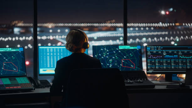 夜の空港タワーでの通話でヘッドセットを持つ女性航空管制官が話します。オフィスルームは、ナビゲーション画面、チームのための飛行機のフライトレーダーデータとデスクトップコンピ� - air traffic control tower ストックフォトと画像
