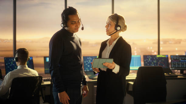 Female and Male Air Traffic Controllers with Headsets Talk in Airport Tower. Office Room Full of Desktop Computer Displays with Navigation Screens, Airplane Flight Radar Data for Controllers. Female and Male Air Traffic Controllers with Headsets Talk in Airport Tower. Office Room Full of Desktop Computer Displays with Navigation Screens, Airplane Flight Radar Data for Controllers. atc stock pictures, royalty-free photos & images