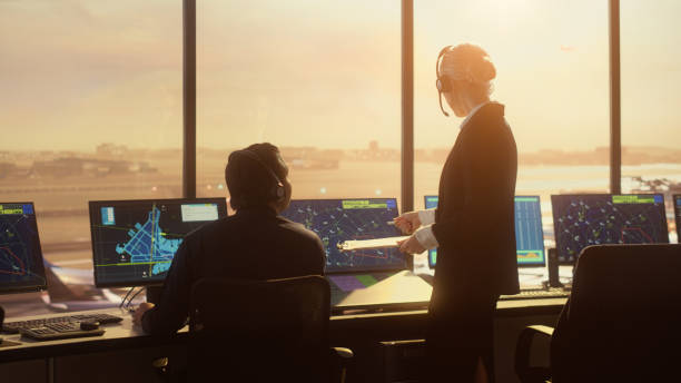 squadra di controllo del traffico aereo diversificata che lavora nella moderna torre dell'aeroporto al tramonto. i controllori celebrano il primo decollo di un nuovo aereo commerciale battendo le mani in una stanza piena di computer. - air traffic control tower foto e immagini stock