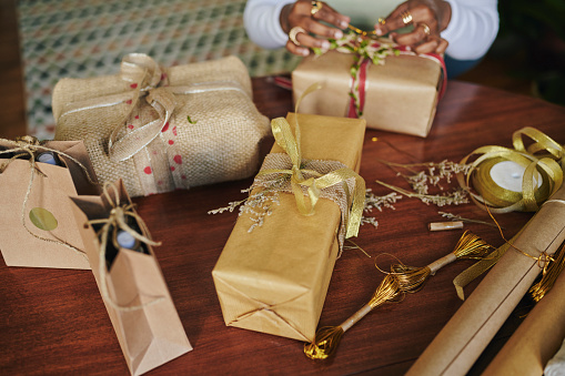 Close-up of a young woman using recycled paper and ribbons to wrap Christmas gifts at a table at home for the holidays