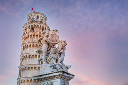 Statue of angels on Square of Miracles in Pisa and Leaning Tower, Italy against colorful sunset sky