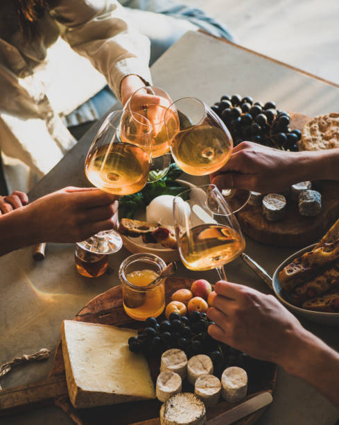 Hands of people clinking glasses with orange or rose wine Hands of people clinking glasses with orange or rose wine over snacks cheese grape bread on concrete background. Gathering, celebrating, wine tasting concept foxys_forest_manufacture stock pictures, royalty-free photos & images