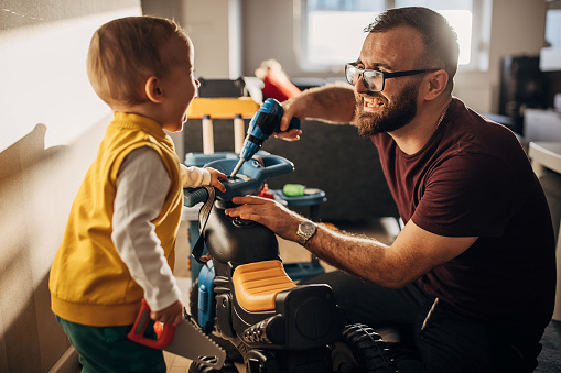 Two people, young father and little son playing with toy tools they are repairing toy motorcycle at home together.