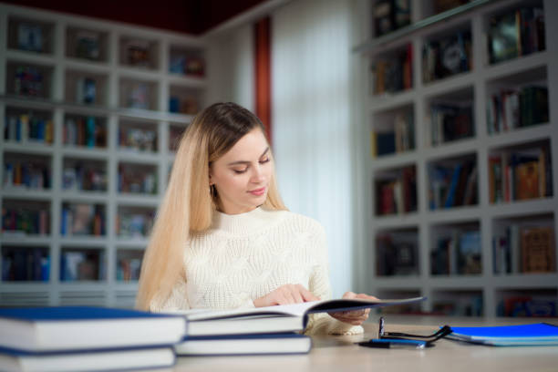 portrait d’un étudiant intelligent avec un livre ouvert le lisant dans la bibliothèque du collège. - book working college student classroom photos et images de collection