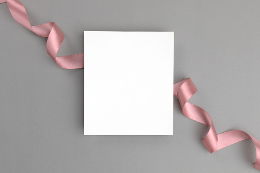 White blank empty card on gray background wrapped with a pink ribbon.