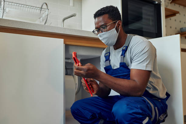 Black plumber with protective face mask fixing sink in customer’s kitchen Black male plumber in uniform fixing kitchen sink. He is squatting and solving the problem african american plumber stock pictures, royalty-free photos & images