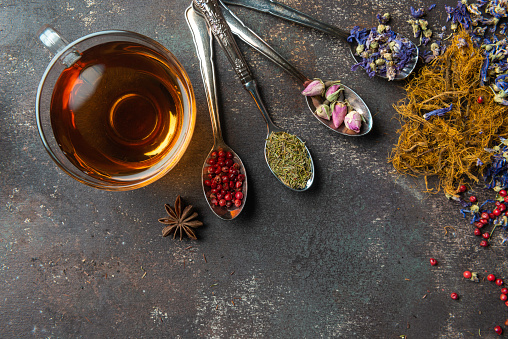 Directly above view of a tea cup. Surrounded by a variety of herbal teas and spices like Purple tea, Rose tea , Anise tea,  Melissa tea, Rosemary tea,  red peppercorns and Rosemary.