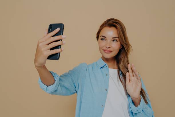 istock Cheerful lady waving at camera on beige background 1348941762