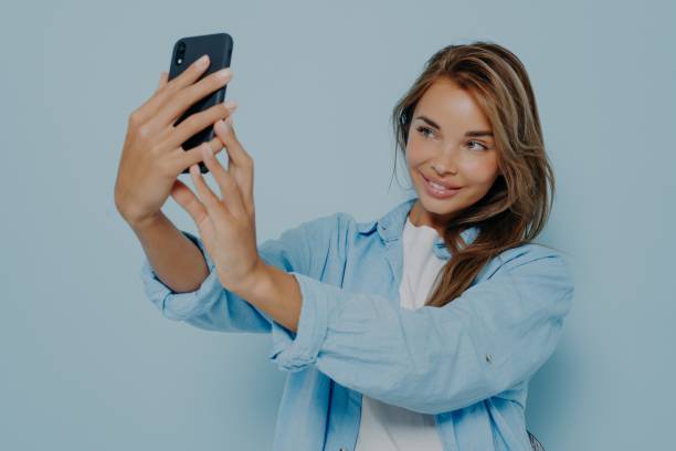 istock Attractive blogger taking selfie near light blue wall 1348941832
