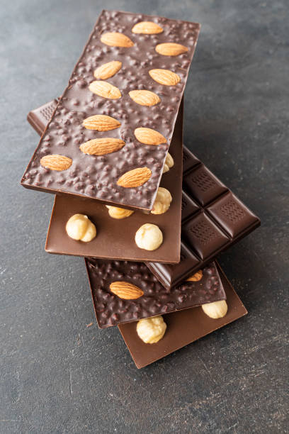 istock assortment chocolate bars with almonds, hazelnuts, handmade sweets. Composition of bars milk and dark almond chocolates hazelnuts on a black background, top view. Pastry craft on the table for chocolate background 1348942408