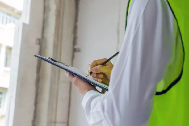 Photo of home inspector engineer in green reflective jacket checking review document and inspecting with clipboard at construction site building interior, construction, contractor and engineering concept