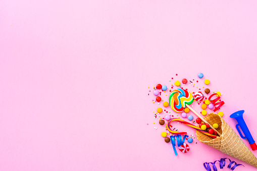 Party, birthday or carnival backgrounds. Overhead view of multi colored items like confetti, candies, drinking straws and streamers shot at the right of pink background leaving useful copy space for text and/or logo. High resolution 42Mp studio digital capture taken with SONY A7rII and Zeiss Batis 40mm F2.0 CF lens